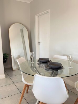 A dining area with a glass table, white chairs, and a large mirror on the wall. - Luxurious 2-Bedroom Apartment in Pretoria with Pool Access (Pretoria)