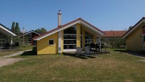 A yellow building with a red roof, a chimney, and a patio with chairs and tables. - Grobenbrode House in der Nähe von Shore (Großenbrode)