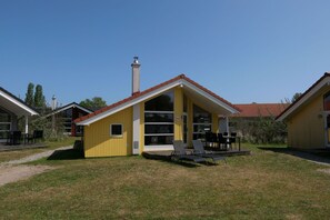 Um edifício amarelo com telhado vermelho, chaminé e um pátio com cadeiras e mesas.