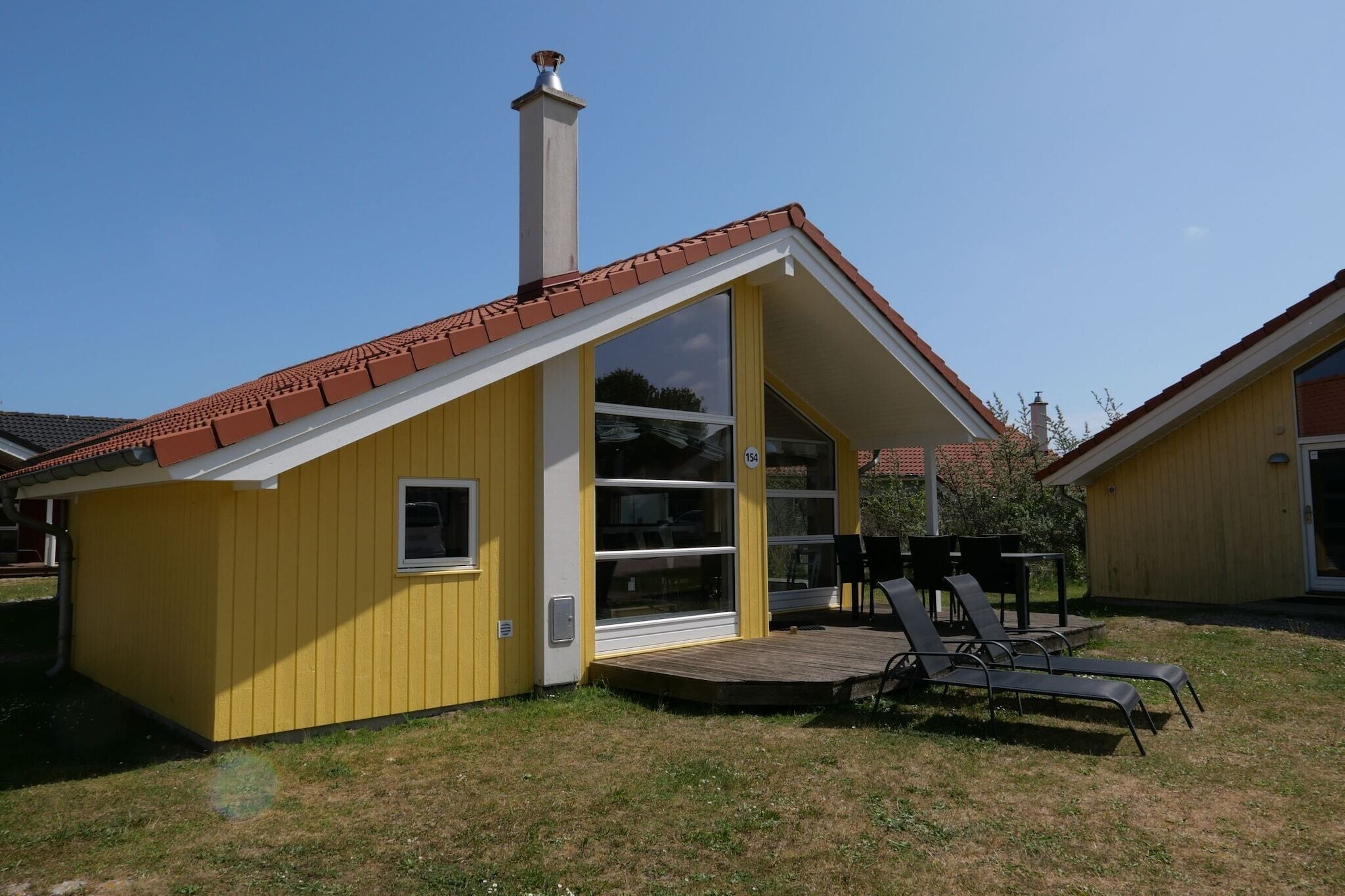 Um edifício amarelo com telhado de telhas vermelhas, chaminé e um alpendre com área de estar externa.
