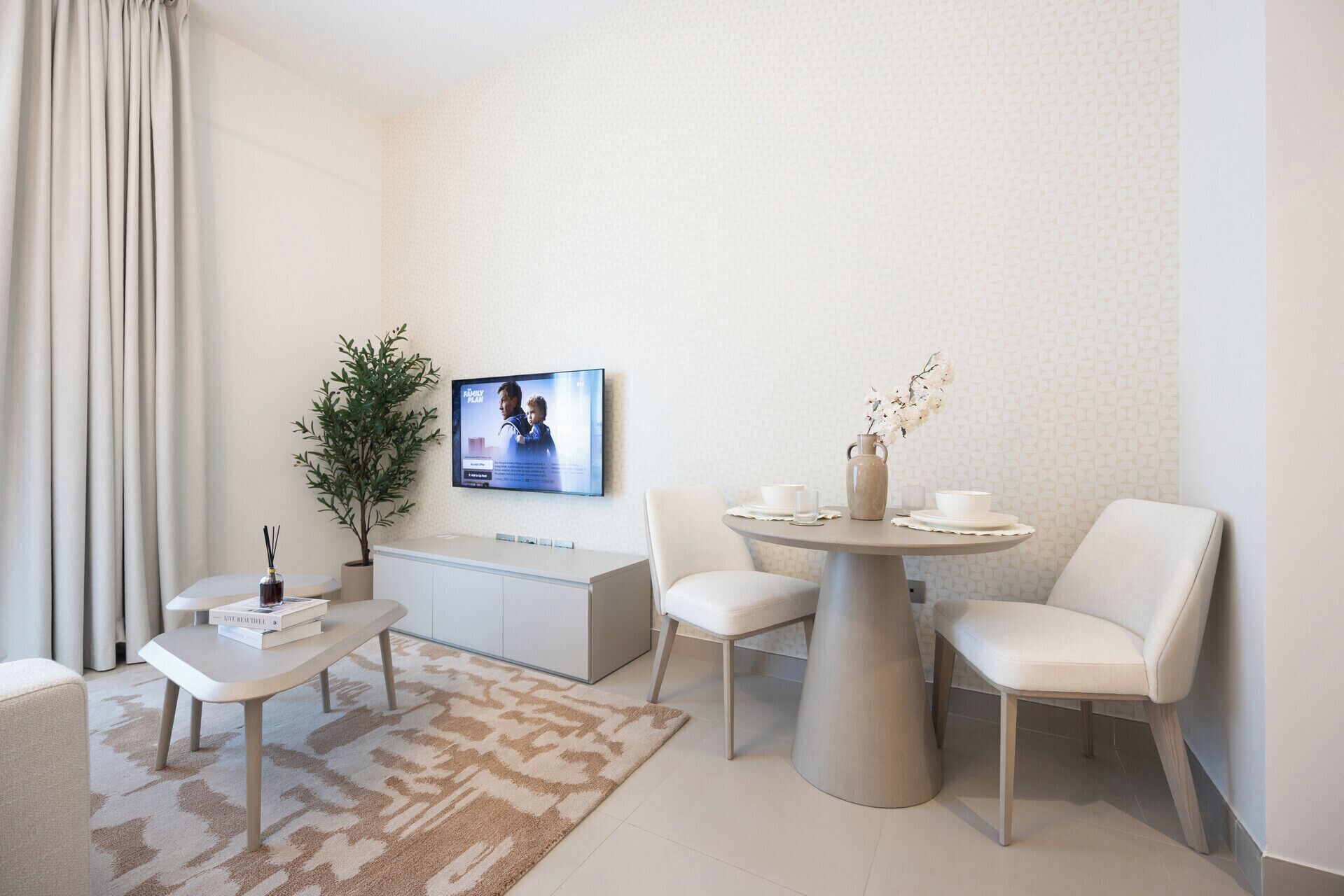 Un salon moderne comprenant un téléviseur à écran plat, une table à manger avec des chaises, un canapé, une petite table d’appoint, une plante en pot et un vase décoratif.