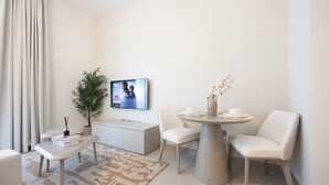 A modern living room with a flat-screen TV, a dining table with chairs, a sofa, a small side table, a potted plant, and a decorative vase. - Bloomfields Studio in Fairways 1 -YGC (Abu Dhabi)