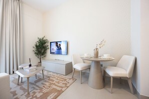 Ein modernes Wohnzimmer mit Fernseher, Esstisch mit Stühlen, einer Couch, einem kleinen Beistelltisch, einer Topfpflanze und einer dekorativen Vase.
