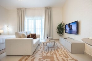 A modern hotel room with a sofa, a coffee table, a TV mounted on the wall, and a large window with curtains. - Bloomfields Studio in Fairways 1 -YGC (Abu Dhabi)