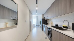 A modern kitchen with a built-in washing machine, a sink, and a dining area visible in the background. - Bloomfields Studio in Fairways 1 -YGC (Abu Dhabi)