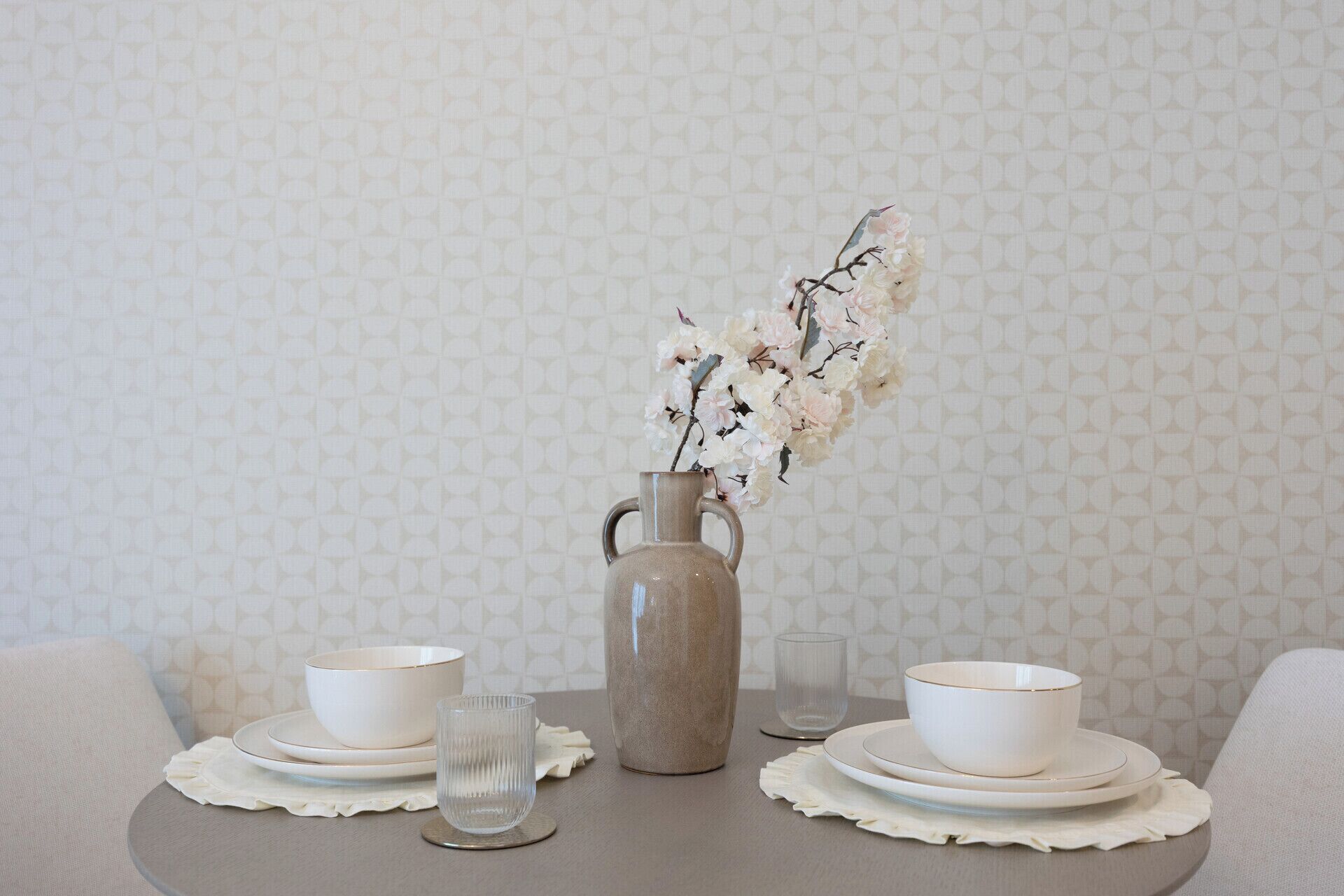 A table set with white plates, bowls, and a clear glass, accompanied by a vase with flowers.