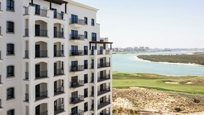 A multi-story building with balconies overlooking a coastal area with a golf course and water. - Bloomfields Studio in Fairways 1 -YGC (Abu Dhabi)