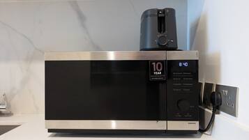 A stainless steel microwave oven with a digital display, a 10-year warranty badge, and a power cord plugged in.