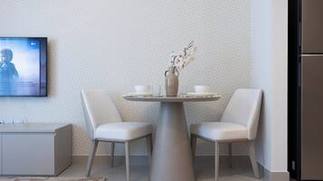 Eine moderne Küche mit einem runden Esstisch, zwei Stühlen, einer Vase mit Blumen und einem flachbildfernseher an der Wand.