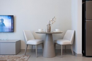 Uma cozinha moderna com uma mesa de jantar redonda, duas cadeiras, um vaso com flores e uma televisão de tela plana na parede.
