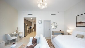 A modern hotel room with a bed, a desk, a chair, a sofa, a dining table, and a kitchen area in the background. - Bloomfields Studio in Fairways 1 -YGC (Abu Dhabi)