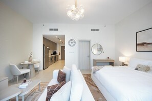 Ein modernes Hotelzimmer mit einem Bett, einem Schreibtisch, einem Stuhl, einer Couch, einem Esstisch und einer Küchenzeile im Hintergrund.