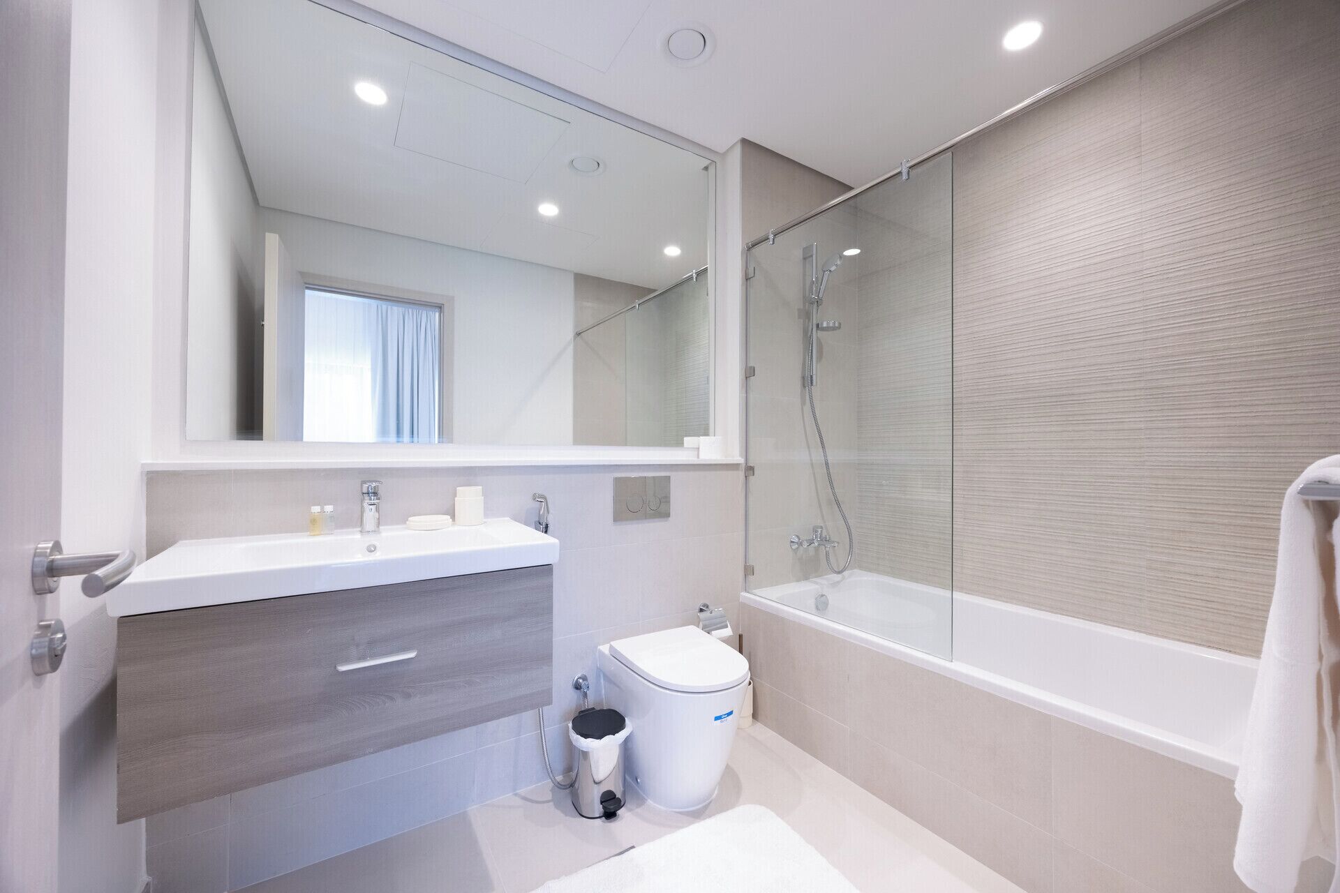 Un baño moderno con un espejo grande, una bañera y un inodoro.