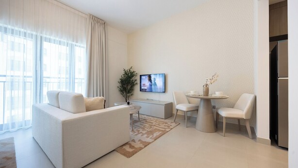 A modern living room with a sofa, a coffee table, and a TV mounted on the wall. - Bloomfields Studio in Fairways 1 -YGC (Abu Dhabi)