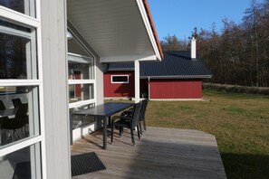 A deck with a table and chairs, a red building in the background, and a clear sky. - Grobenbrode Spa Haus für 8 (Großenbrode)
