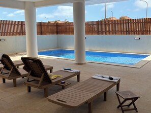Un espace aménagé au bord de la piscine, avec des chaises longues, une petite table et une piscine.