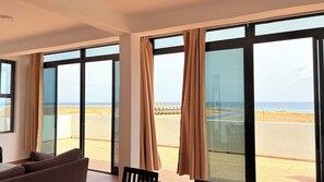 Une pièce dotée de grandes fenêtres, d’un plancher en bois et offrant une vue sur la plage.