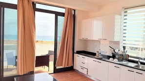 Eine moderne Küche mit Blick auf den Strand, ein Essbereich mit Stühlen und eine Glastür zum Aufschieben.