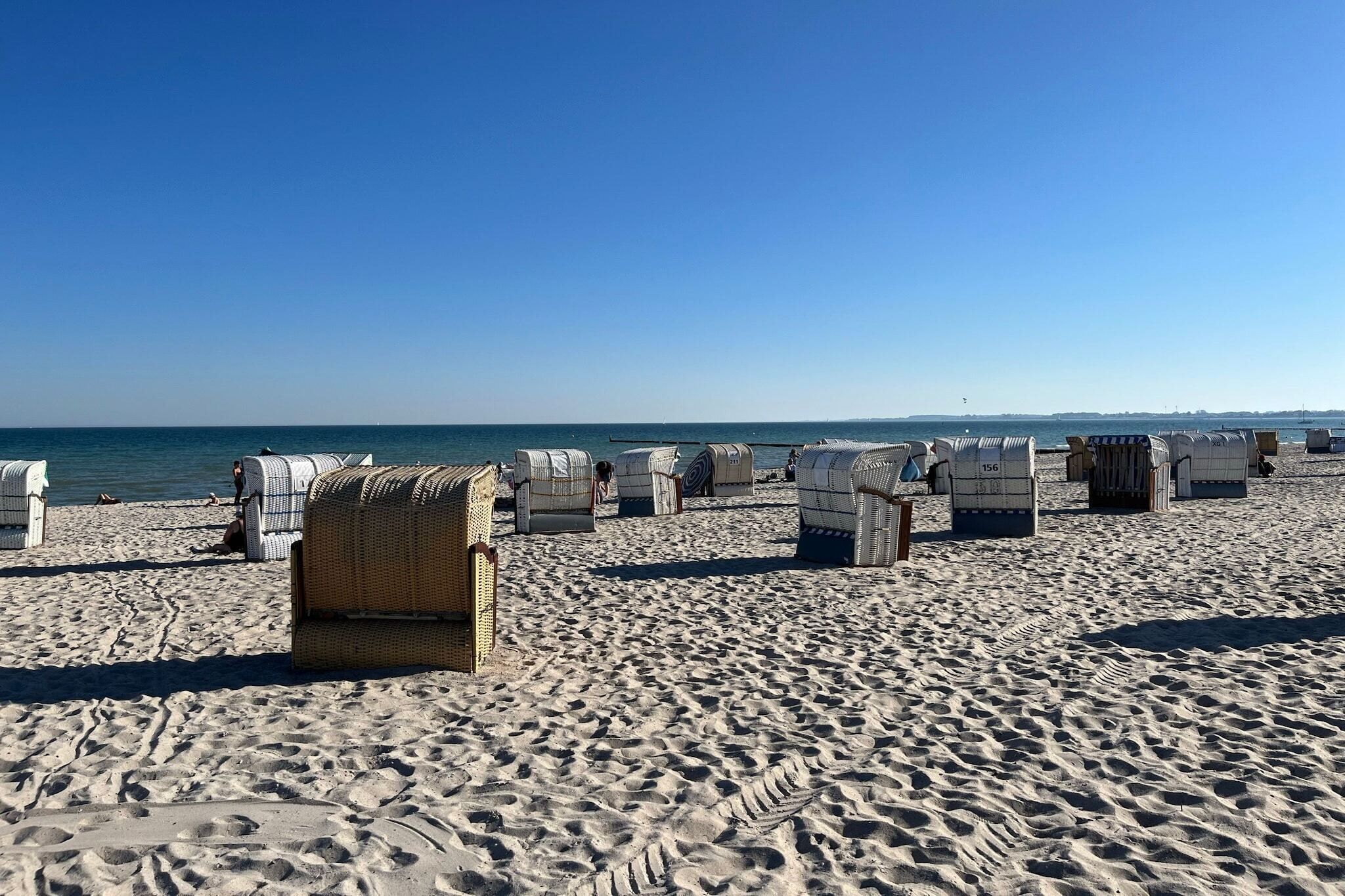 Ein Strand mit Reihen aus Korbstühlen und Sonnenschirmen, feinem Sand und dem Meer im Hintergrund.