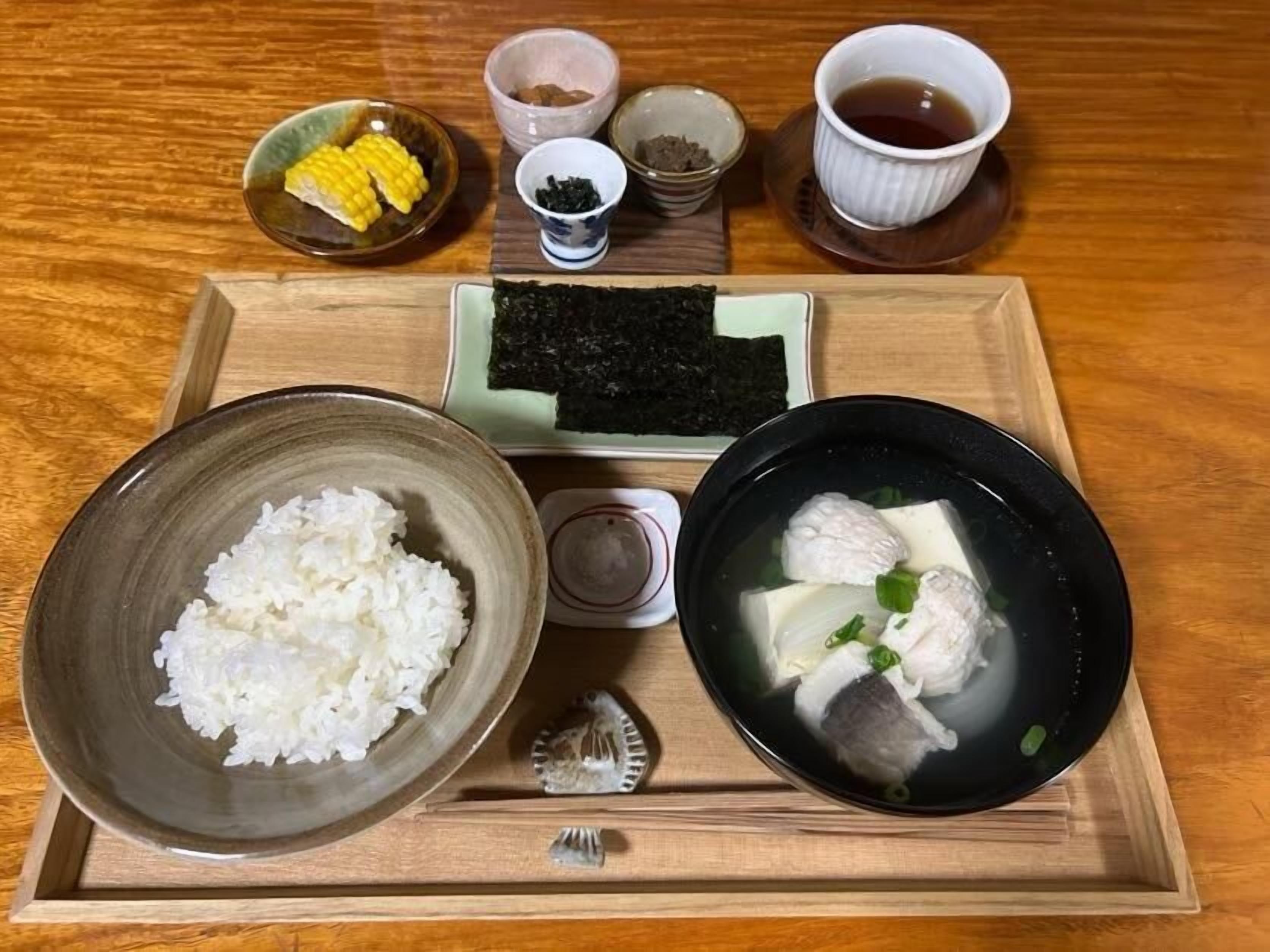 Una bandeja con un tazón de arroz, un tazón de sopa de pescado, un pequeño tazón de maíz y una taza de té.