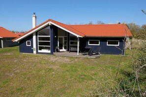 A two-story house with a red-tiled roof, a chimney, and a covered porch with outdoor seating. - Grobenbrode-Kiefernschutzgebiet (Großenbrode)