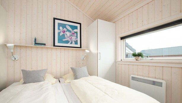Quarto com cama, almofadas, um quadro emoldurado, janela e radiador.