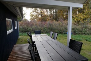 Eine Terrasse im Freien mit einem Holztisch und Stühlen, umgeben von einem Garten mit Bäumen und Sträuchern.