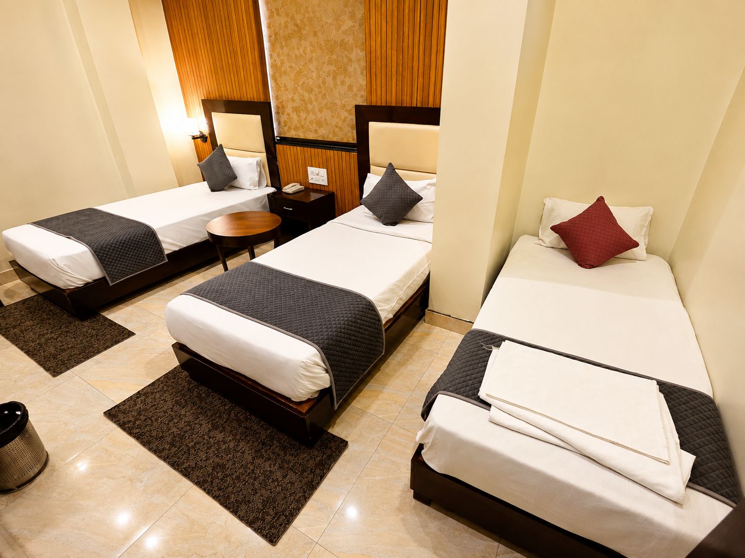 A hotel room with two single beds, a small table, and a trash bin.