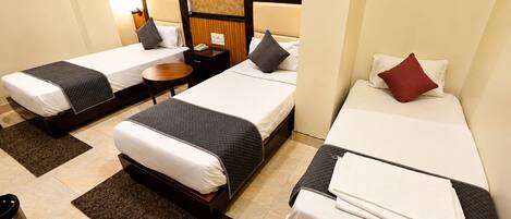 A hotel room with two single beds, a small table, and a trash bin.