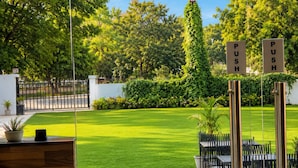 An outdoor seating area with tables and chairs, a sign indicating an exit, and a hedge in the background. - Hote Elvora (Jaipur)