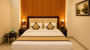A hotel room with a large bed, two bedside tables, a nightstand, a wall-mounted lamp, and a framed picture on the wall. - Hote Elvora (Jaipur)