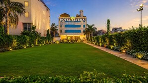 A modern hotel with a flat roof, a central entrance, and a well-maintained lawn. - Hote Elvora (Jaipur)