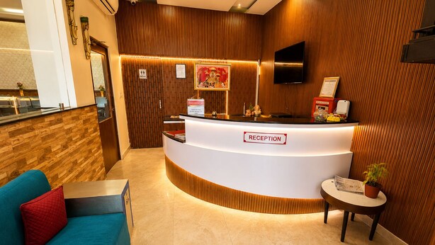A reception area with a wooden reception desk, a sofa, and a small table with a plant. - Hote Elvora (Jaipur)