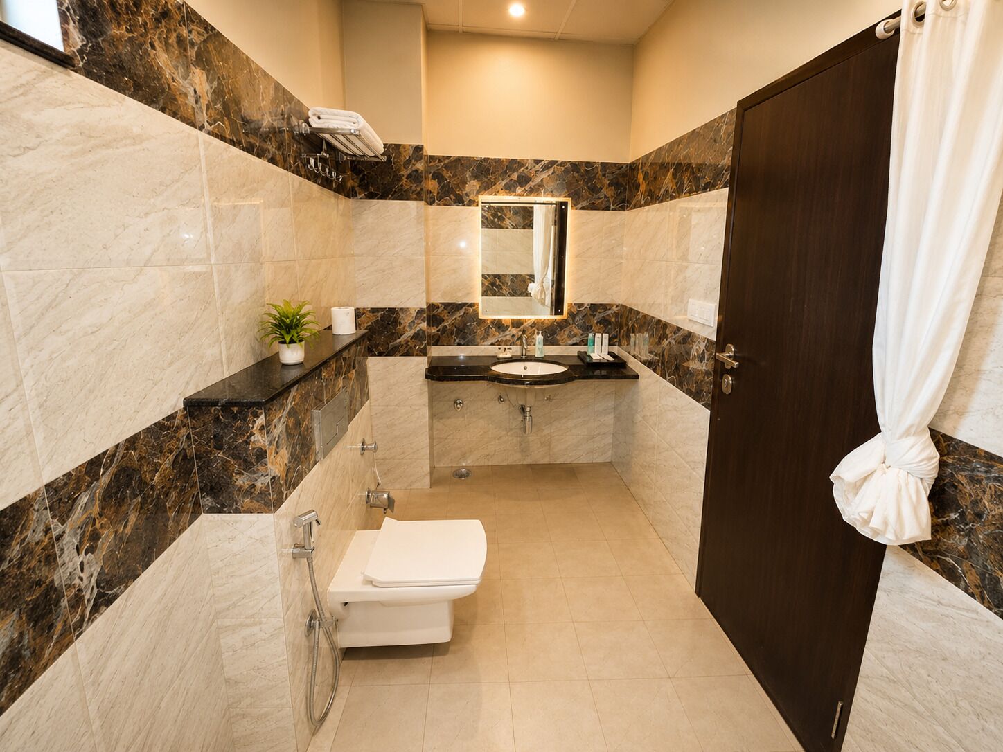 Un bany amb una paret de marbre, un lavabo, un vàter i una dutxa.