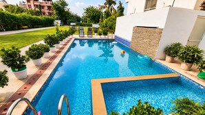 A swimming pool with a clear blue water surface, surrounded by potted plants and a few lounge chairs. - Hote Elvora (Jaipur)