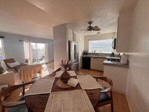 A modern kitchen with a dining area, large windows, and a ceiling fan.