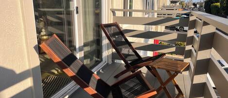 En balkon med to træloungestole, et lille bord og udsigt til palmer og en gade.