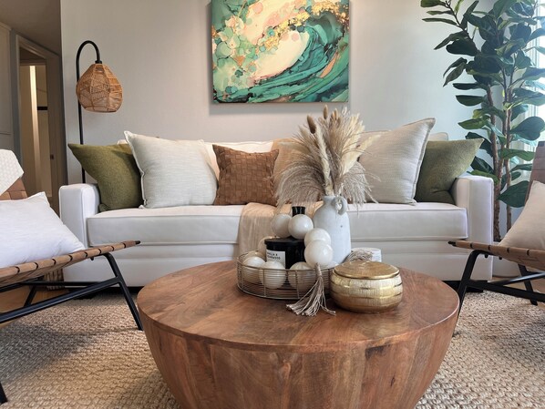 A living room with a white sofa, a round wooden coffee table, and a painting on the wall.