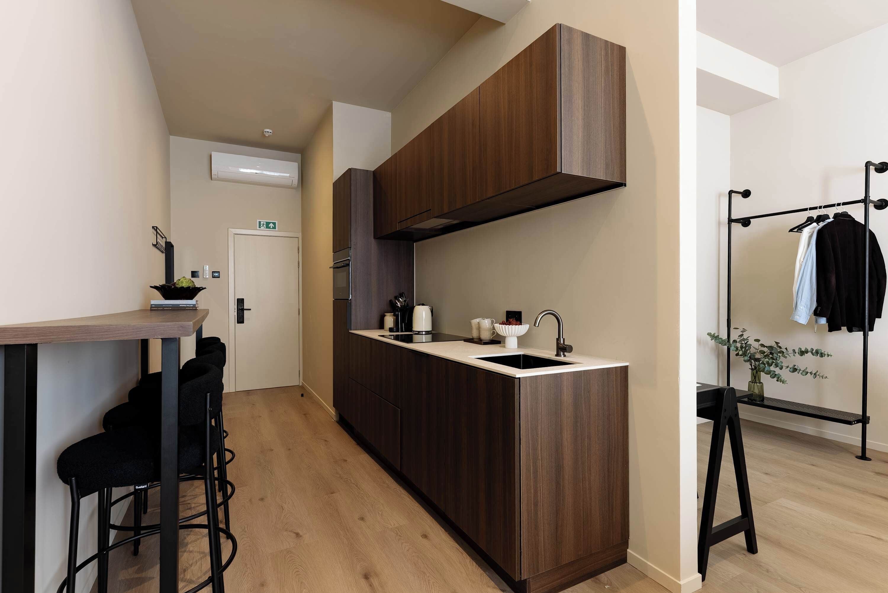 Une cuisine moderne avec des meubles en bois foncé, un plan de travail blanc et un robinet noir. On y trouve un petit îlot central avec un évier et une machine à café.