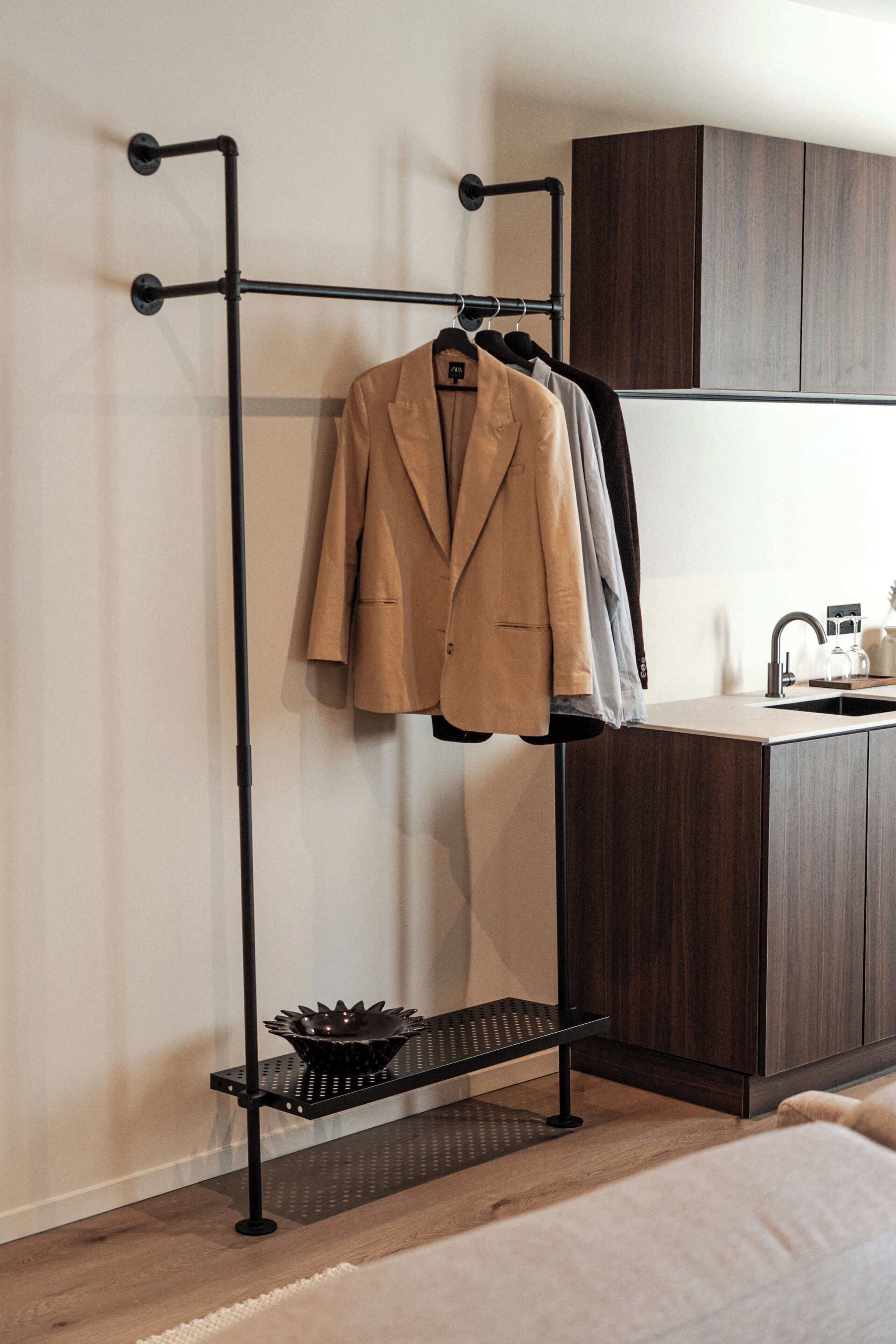 A metal coat rack with a beige coat hanging, a black bowl on a shelf, and a kitchen area with dark wooden cabinets.