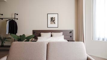 A modern bedroom with a bed, bedside tables, a wall-mounted artwork, a clothing rack, and a potted plant.