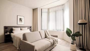 A modern hotel room with a bed, a sofa, a bedside table, a lamp, and a window with curtains.