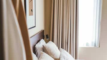 Une chambre d’hôtel avec un lit, des oreillers, une tête de lit, une table de chevet, une lampe, une fenêtre avec des rideaux et un tableau encadré au mur.