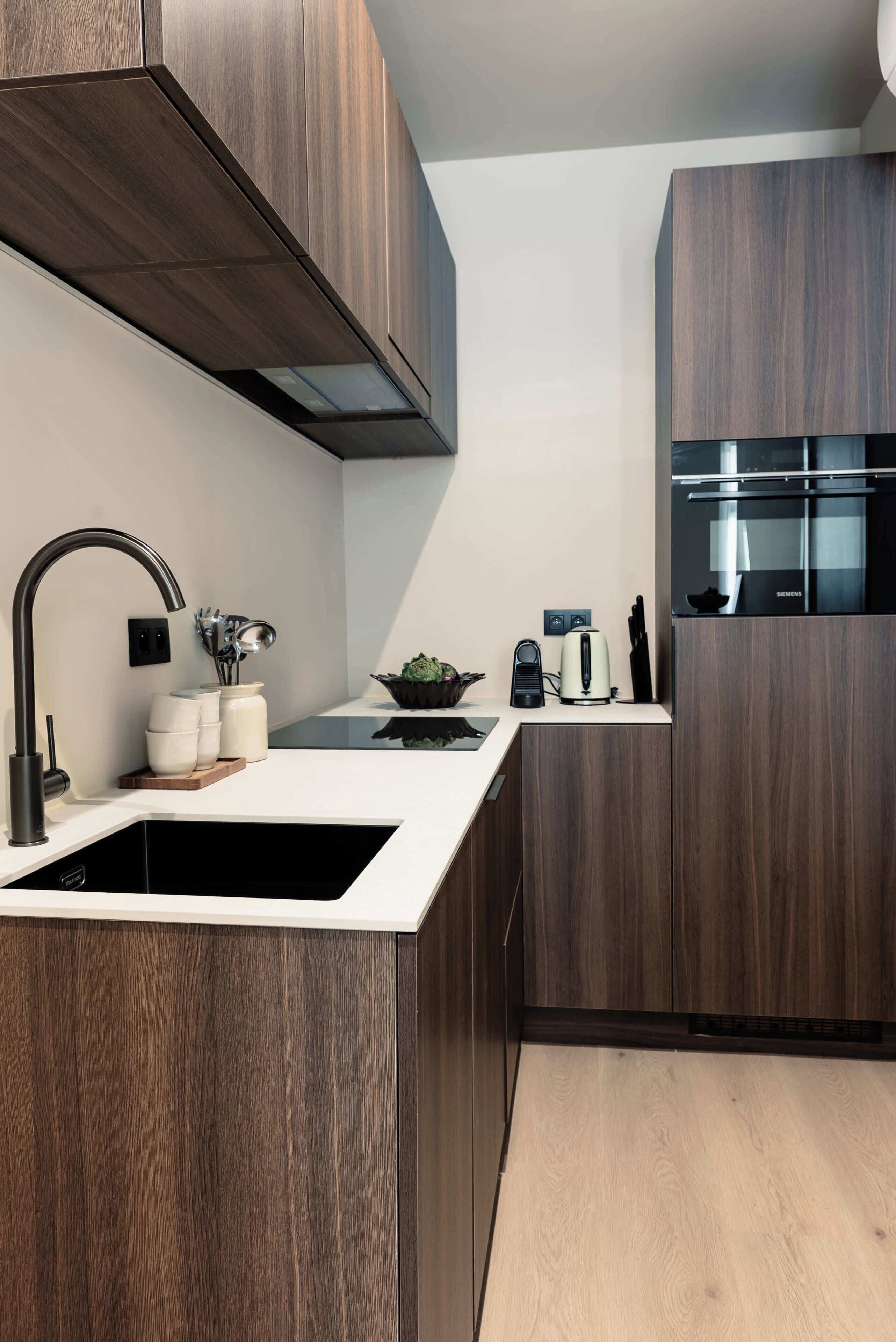 A modern kitchen with dark wood cabinetry, a stainless steel sink, and a built-in oven.