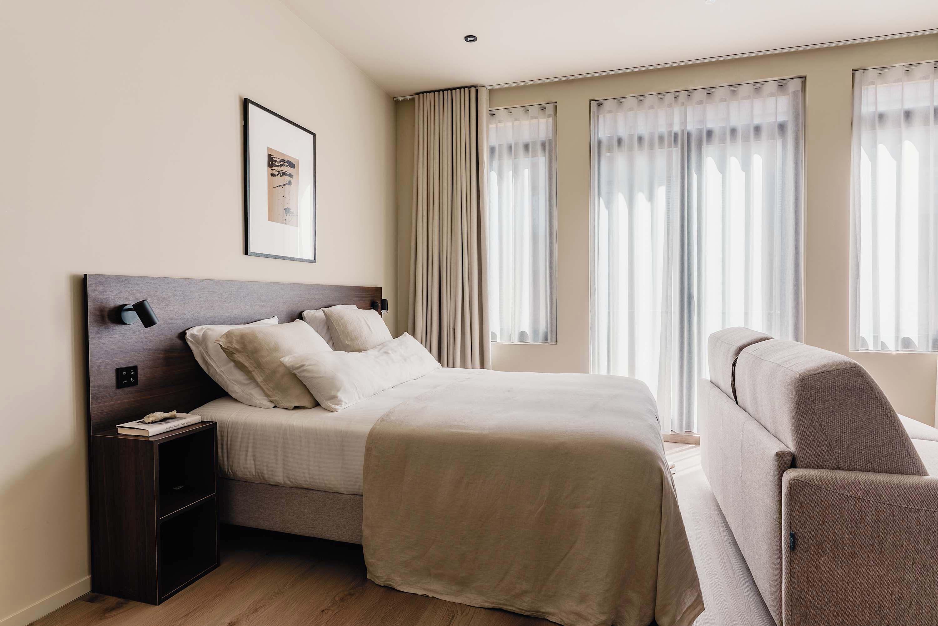A hotel room with a bed, a nightstand, a chair, and a window with curtains.