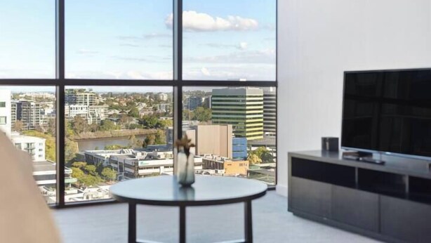 A modern living room with a large window, a round table, and a flat-screen TV.