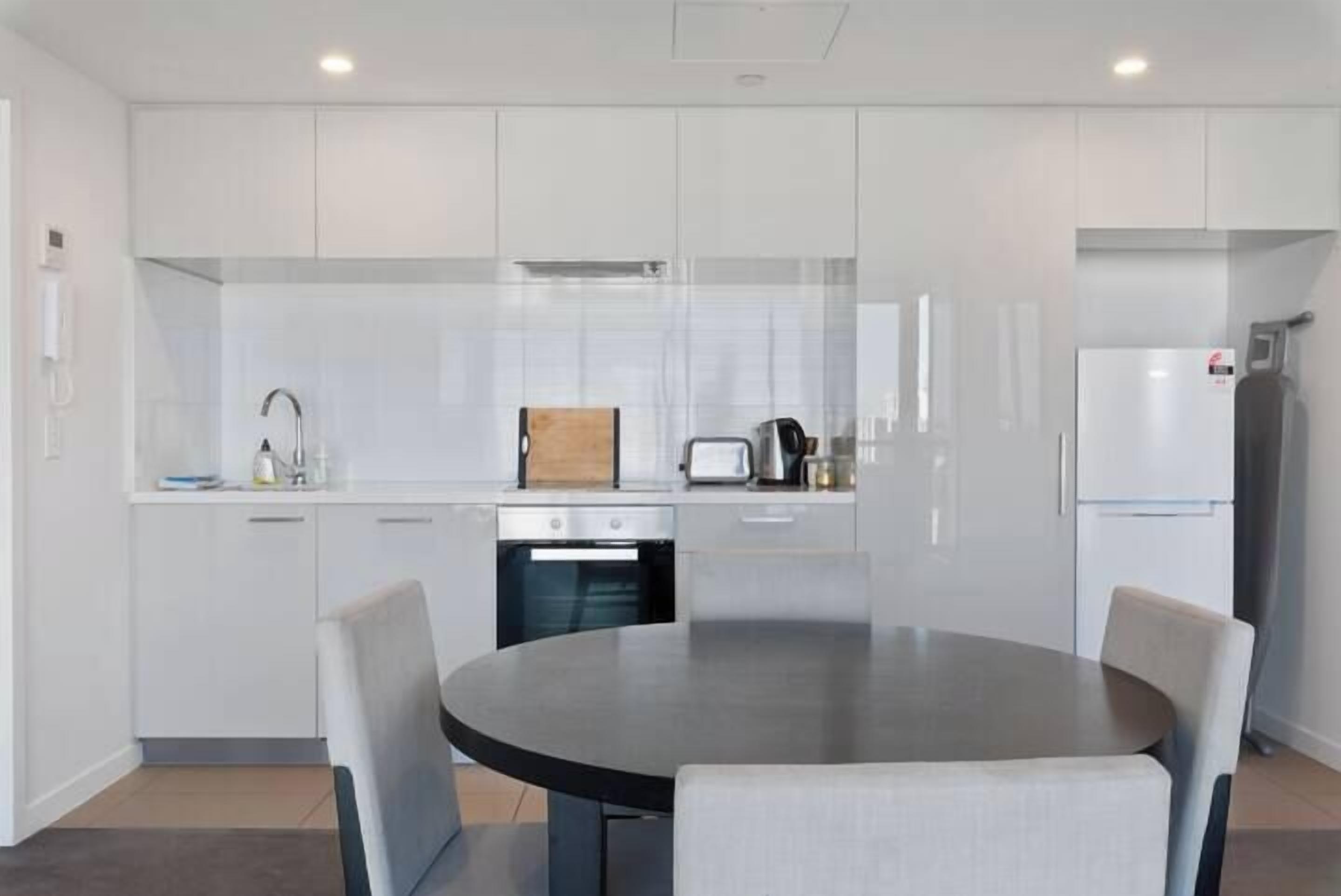 A modern kitchen with white cabinetry, a round dining table, and a built-in oven.