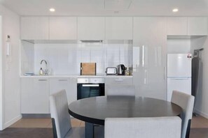 A modern kitchen with white cabinetry, a round dining table, and a built-in oven.