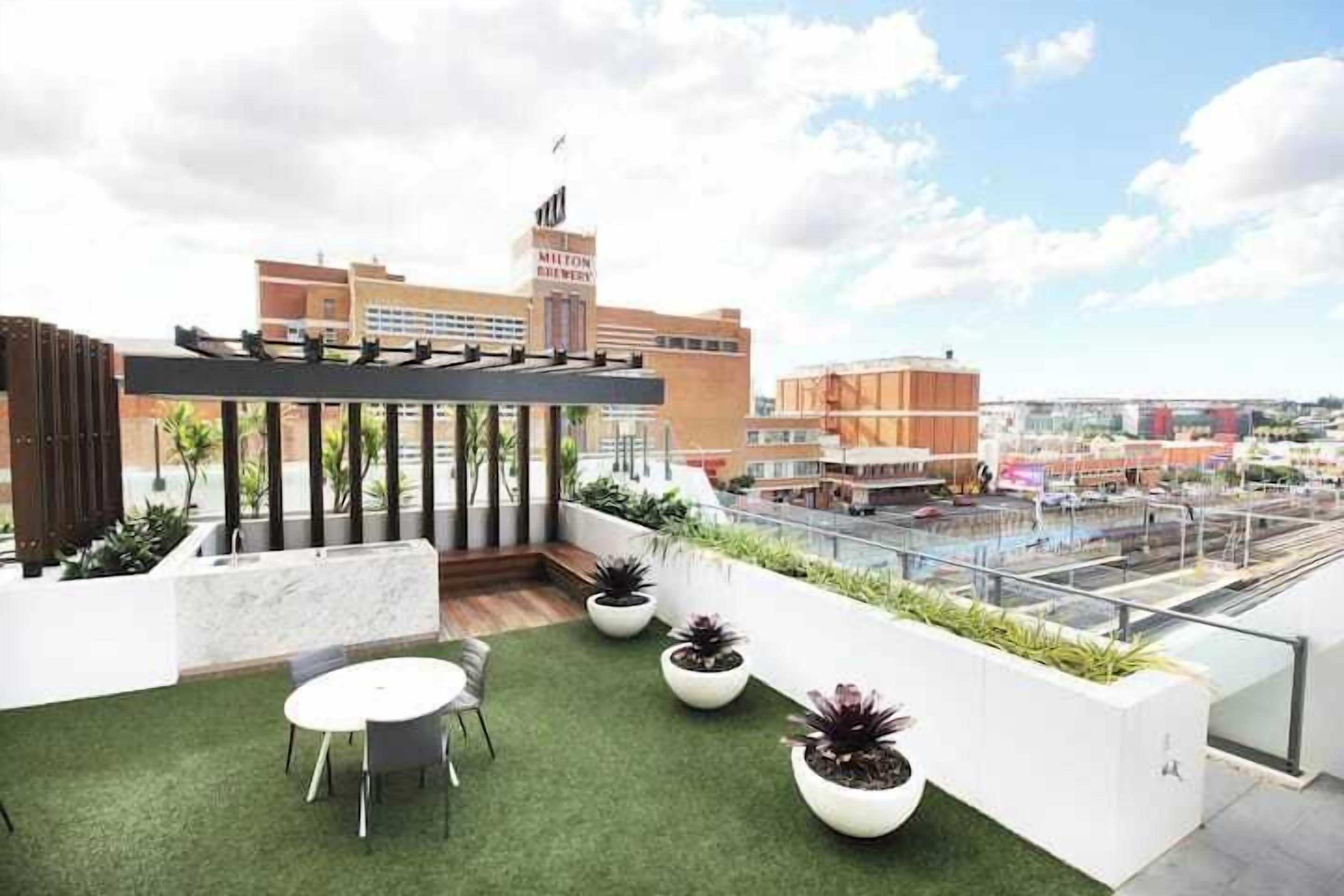 A rooftop terrace with a table and chairs, potted plants, and a view of the cityscape.