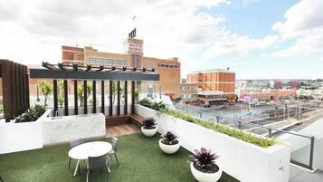 A rooftop terrace with a table and chairs, potted plants, and a view of the cityscape.